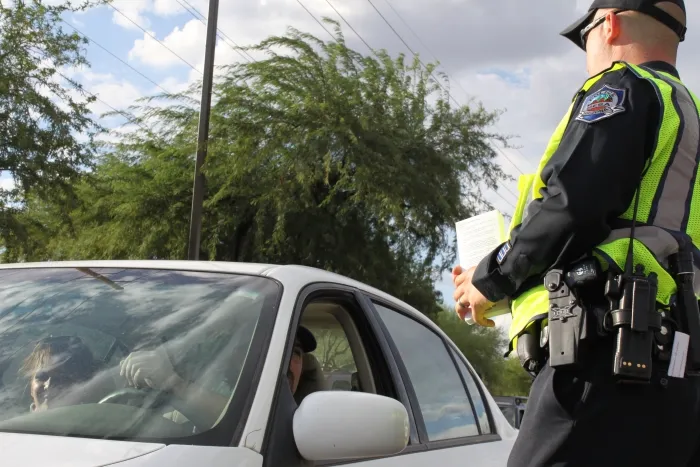 A police officer in a high-visibility vest standing beside a white car during a traffic stop.