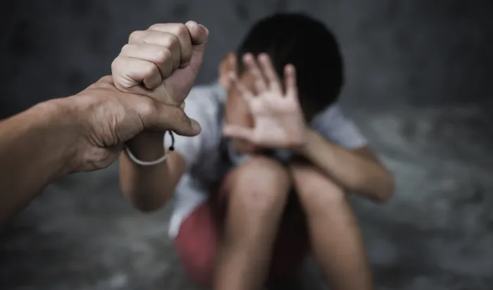 A fearful child cowering in the background while a hand reaches out towards them, symbolizing abuse or neglect.
