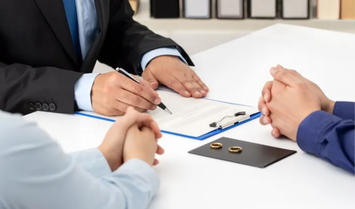 A lawyer reviewing divorce documents with a couple, with wedding rings placed on the table.