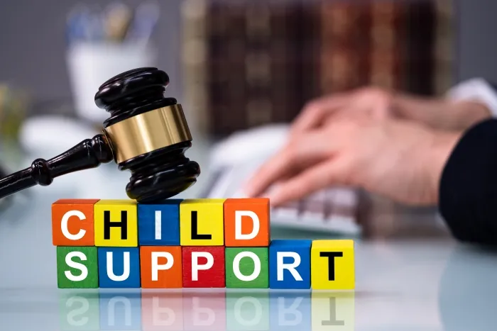 A gavel resting on colorful blocks that spell out "CHILD SUPPORT," with a person working on a computer in the background.