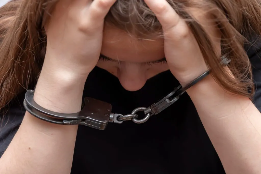 A distressed person with their head in their hands, wearing handcuffs.